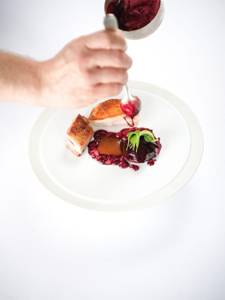 Sauce versée sur une assiette de gibier et fruits rouges, Zostera